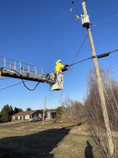 Tinuum line crew securing a fibre splice closure to the messenger strand on a rural pole, New Brunswick